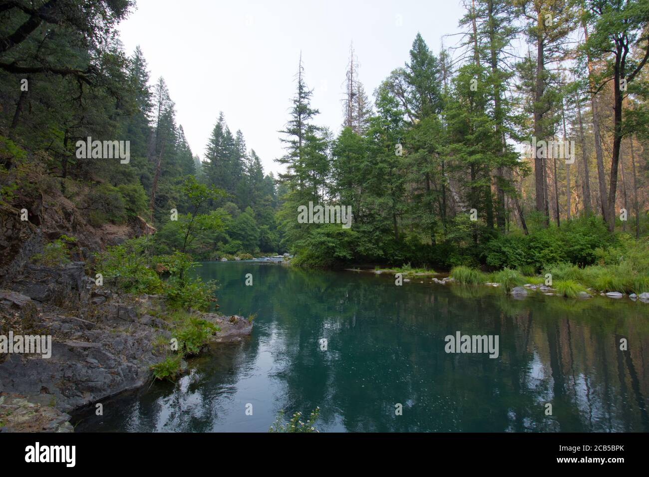 Stagni di acqua blu profondo in fiume con la vegetazione riflessione su superficie d'acqua con una scogliera rocciosa sul lato Foto Stock