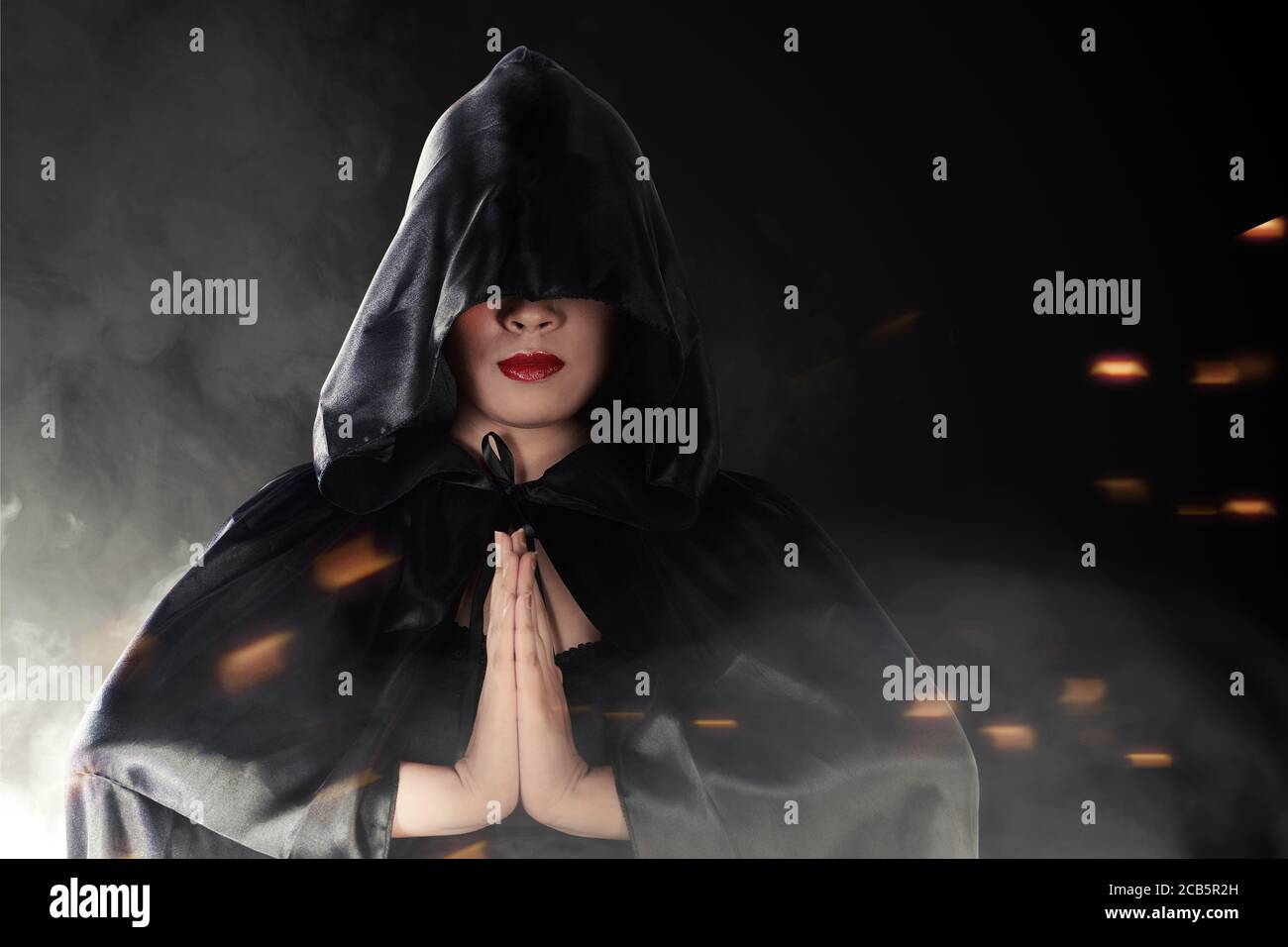 Donna strega asiatica con mantello nero facendo rituale mistico con sfondo nero Foto Stock