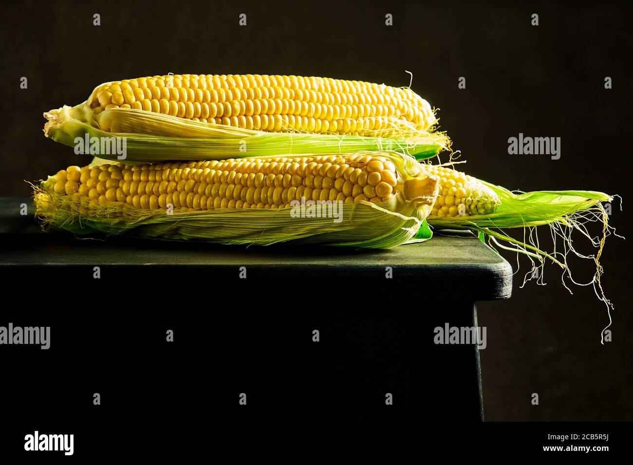 Pannocchie di mais crudo maturo su un tavolo di legno scuro. Cibo sano, pannocchie di mais crudo fresco, stile rustico Foto Stock