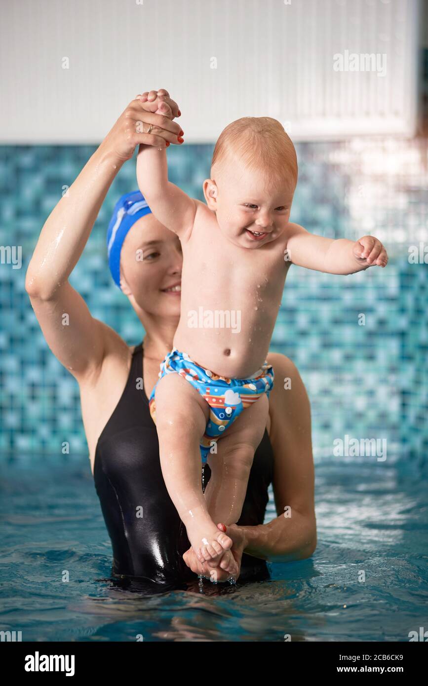 Immagine verticale di una madre sorridente che tiene il suo bambino sull' acqua in piscina durante gli esercizi di nuoto per i bambini. Concetto di  sviluppo precoce Foto stock - Alamy