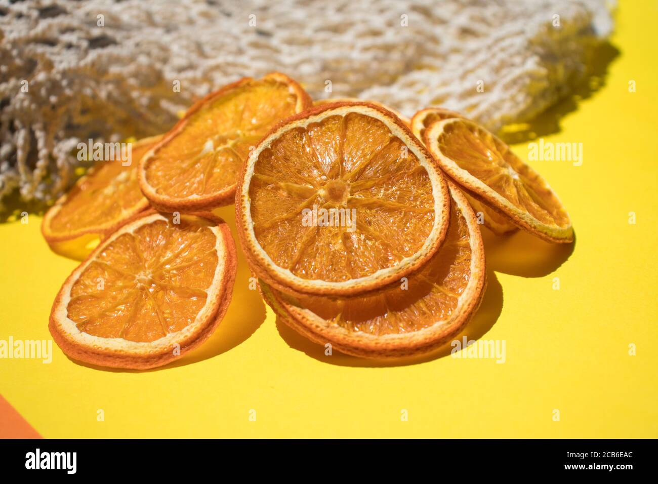 Preparazione a casa. Arancia secca a fette, patatine di frutta naturali senza zucchero e spezie su sfondo giallo. Foto Stock