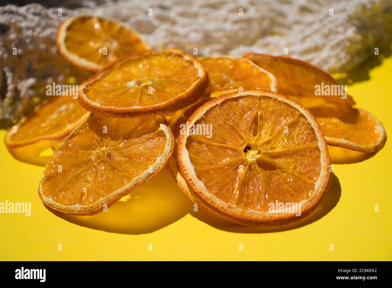 Preparazione a casa. Arancia secca a fette, patatine di frutta naturali senza zucchero e spezie su sfondo giallo. Foto Stock