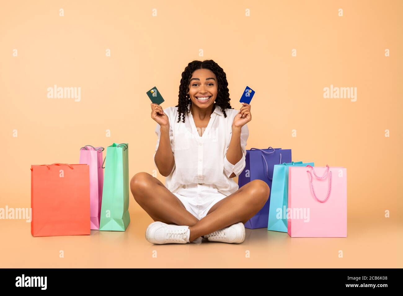 Girl Holding carte di credito seduta tra Shopper Borse, Beige sfondo Foto Stock