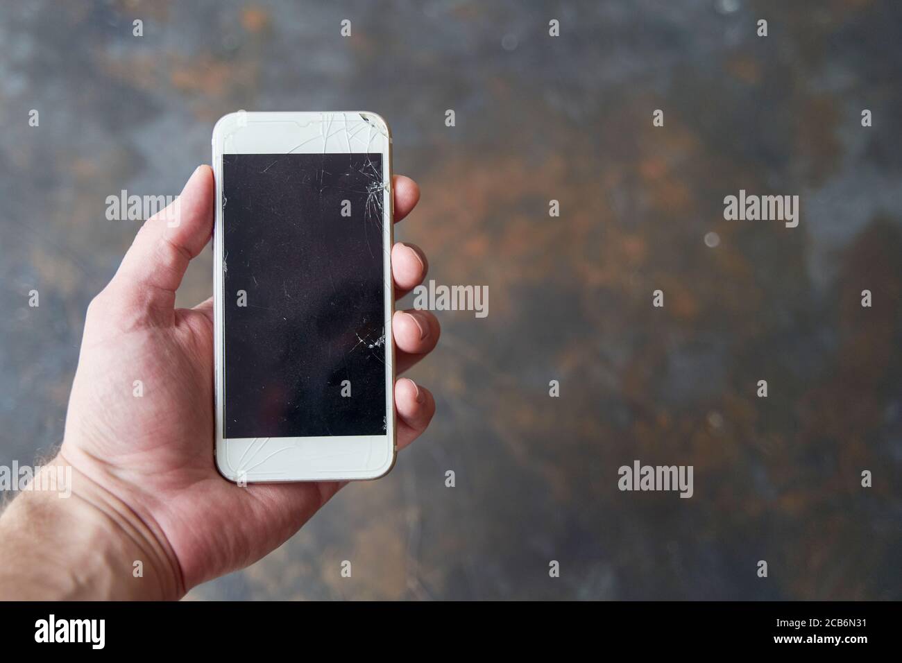 Un giovane tiene uno smartphone con uno schermo rotto in mano su uno sfondo scuro. Derisione Foto Stock