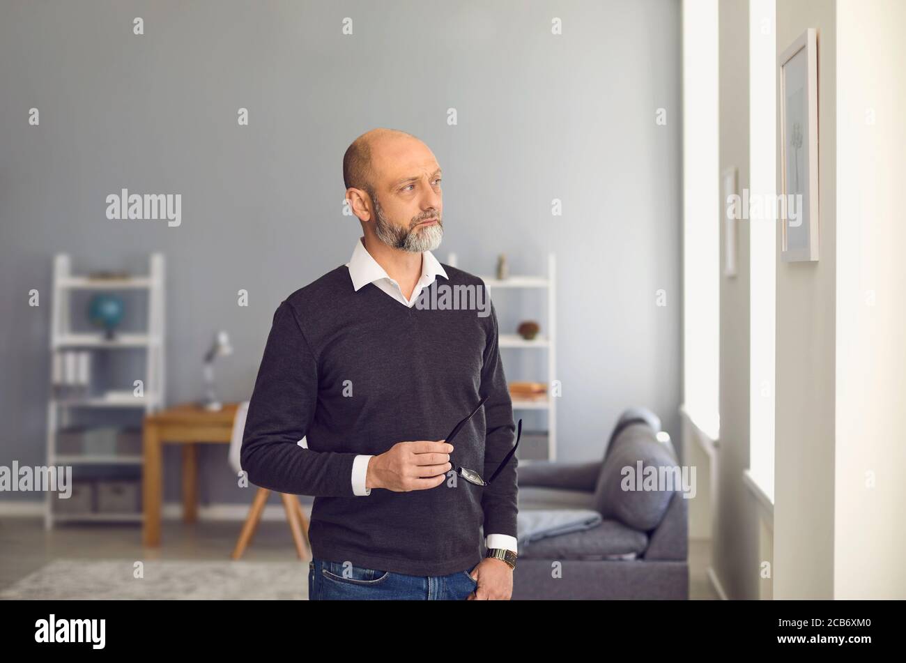 Uomo serio senier con occhiali in piedi guardando lontano mentre si trova in una stanza a casa. Foto Stock