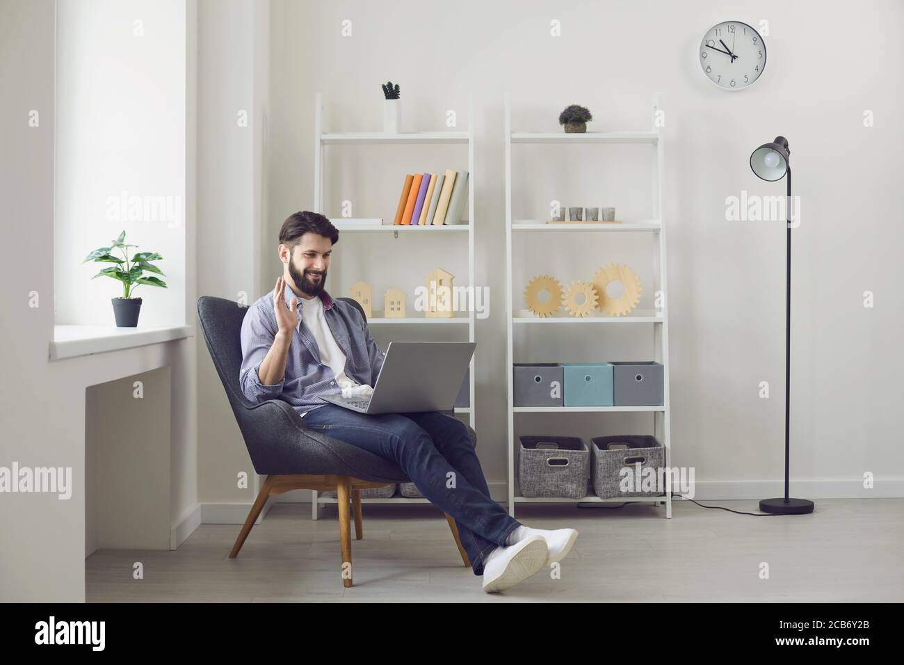 Giovane ragazzo con il portatile che si fa sventolare mentre parla con un amico, un collega o un insegnante online da casa. Comunicazione remota Foto Stock