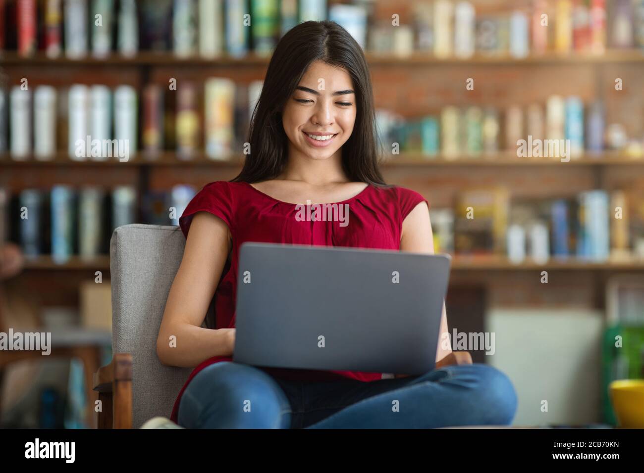 Smiling Asian Student Girl si prepara per l'esame con il laptop alla Biblioteca Foto Stock