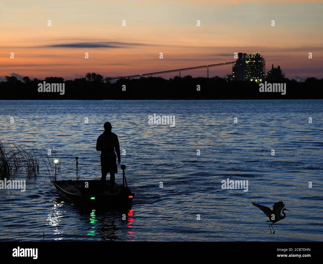 Un pescatore nella sua piccola barca ben attrezzata inizia il suo Pesca di un giorno su un lago della Florida con una splendida alba Foto Stock