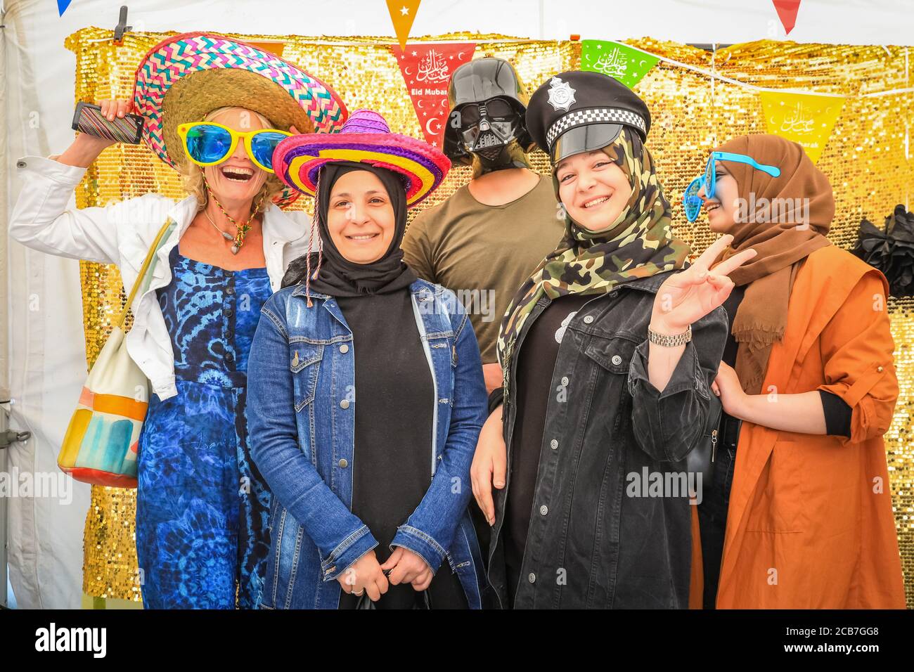 Un gruppo di donne si diverte con lo stand fotografico "cappelli di fede" all'Eid Festival di Trafalgar Square, Londra, Inghilterra Foto Stock