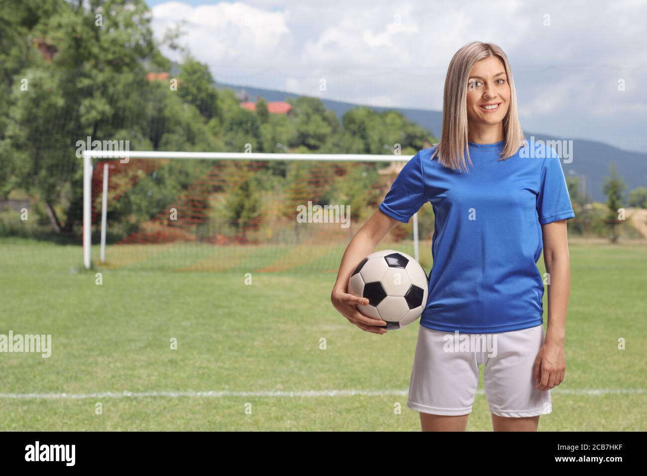 Calciatrice femminile che tiene una palla sotto il braccio e in piedi su un campo da calcio Foto Stock