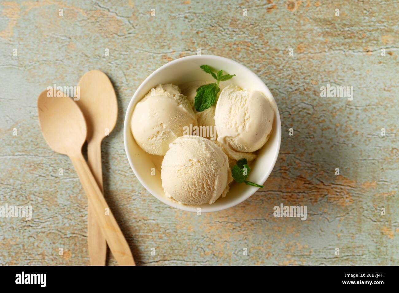 Vista dall'alto di una tazza di gelato alla vaniglia in bianco ciotola su sfondo rustico pastello Foto Stock