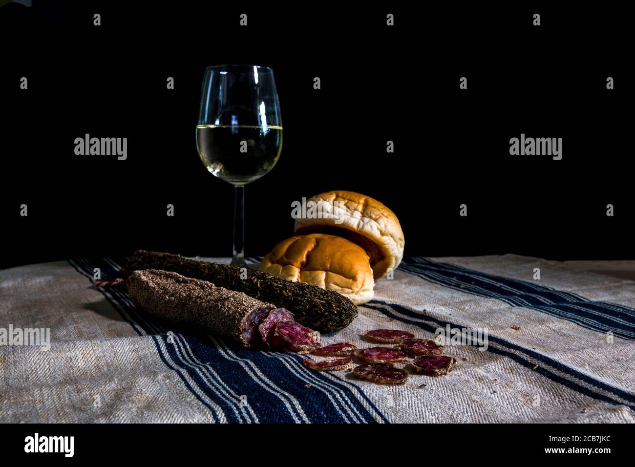 ancora da tavola con un bicchiere di vino bianco assortito asciugare le salsicce e il pane su un panno di farina di colore blu strisce Foto Stock