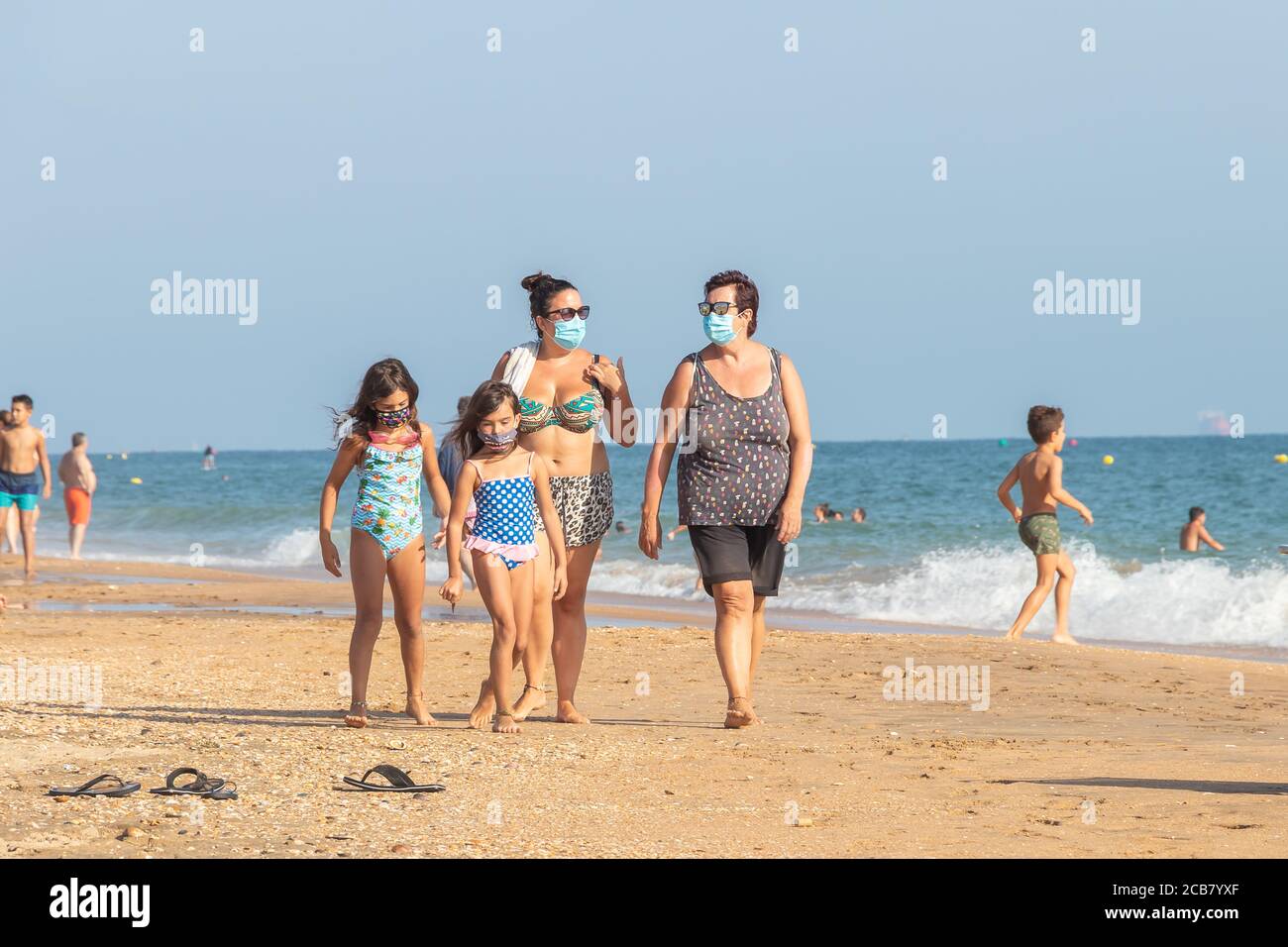 Punta Umbria, Huelva, Spagna - 7 agosto 2020: Passeggiata in famiglia in spiaggia con maschere protettive o mediche. Nuova normalità in Spagna con sociale di Foto Stock