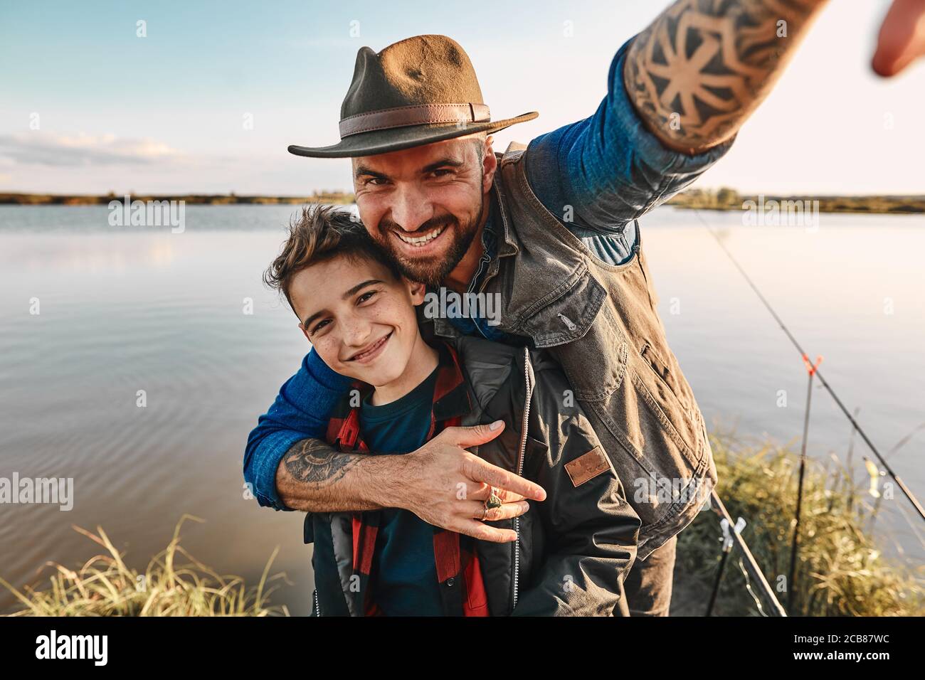 Padre abbraccerà il figlio e prende selfie, che si leverà sul tavolo a casa come foto per la memoria. Loro Buon divertimento. Sfondo lago. Foto Stock