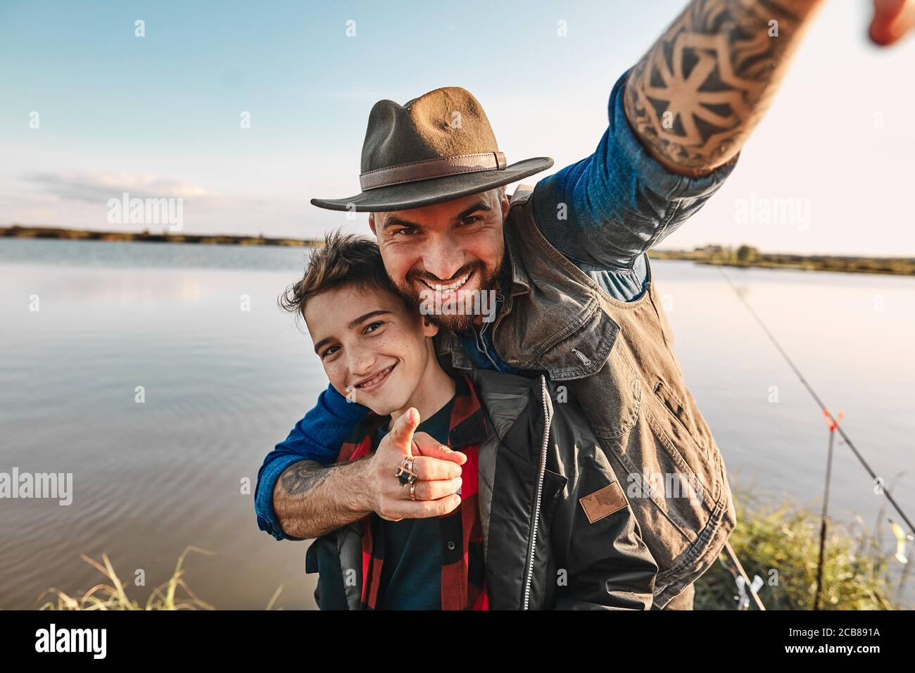 Padre abbraccerà il figlio e prende selfie, che si leverà sul tavolo a casa come foto per la memoria. Loro Buon divertimento. Sfondo lago. Foto Stock