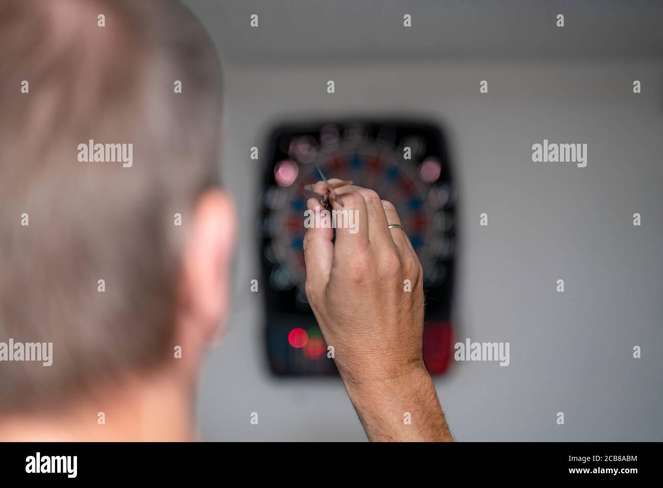 Un uomo biondo di 50 anni gioca freccette. Una macchina a freccette elettrica mostra i suoi colpi in un duello. Il dartboard è appeso in una cantina di festa. Foto Stock