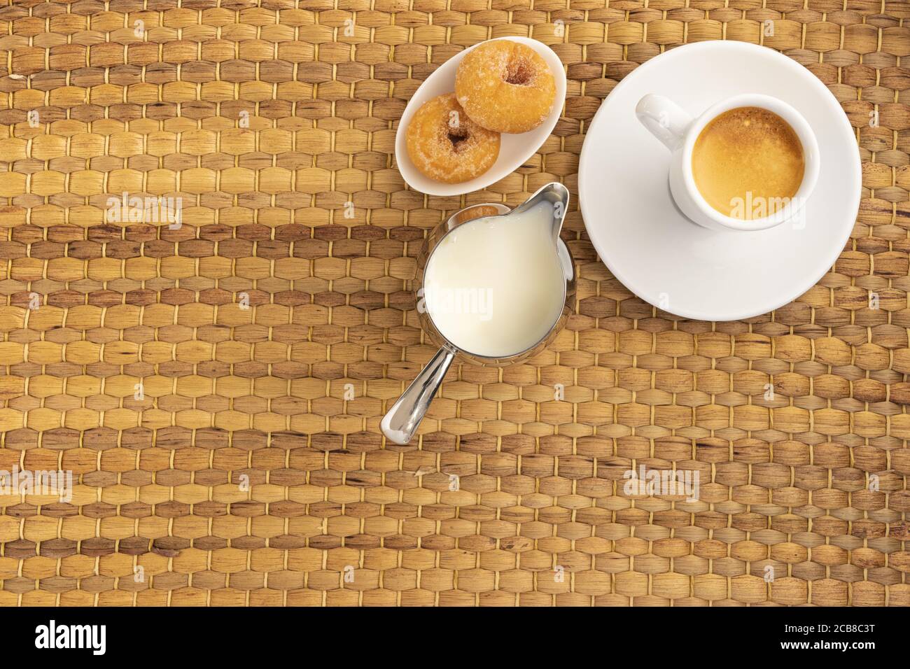 Colpo ad angolo alto di una tazza di caffè, ciambelle e una caraffa di latte su una superficie tessuta Foto Stock