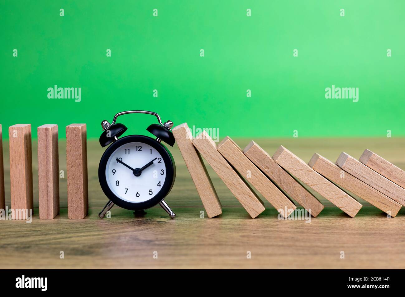concetto di effetto domino con piastrelle di legno bloccate da orologio con sfondo verde Foto Stock