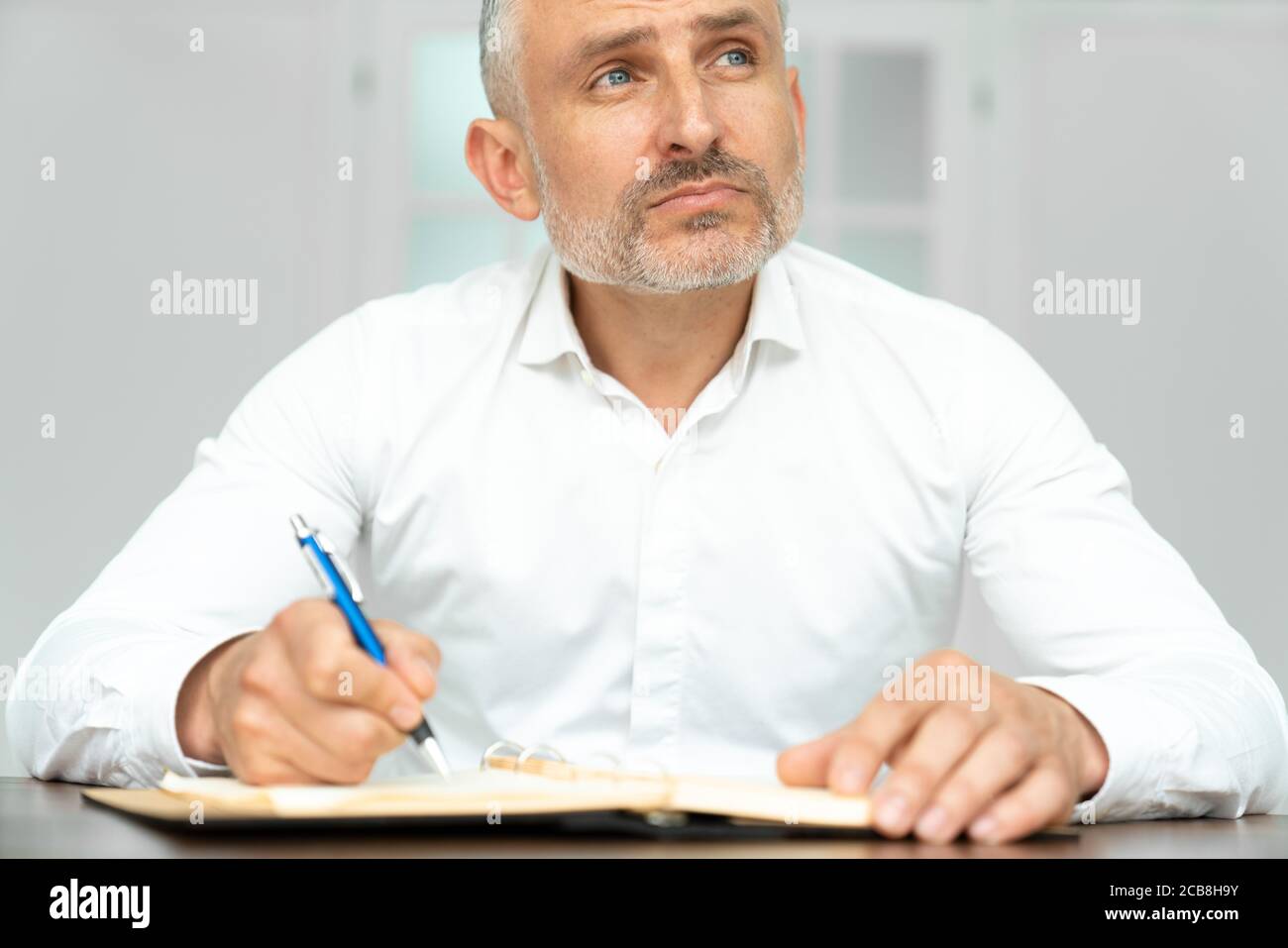 Dal basso di un elettricista etnico carismatico in camicia bianca con la penna in mano che crea un progetto sul posto di lavoro Foto Stock