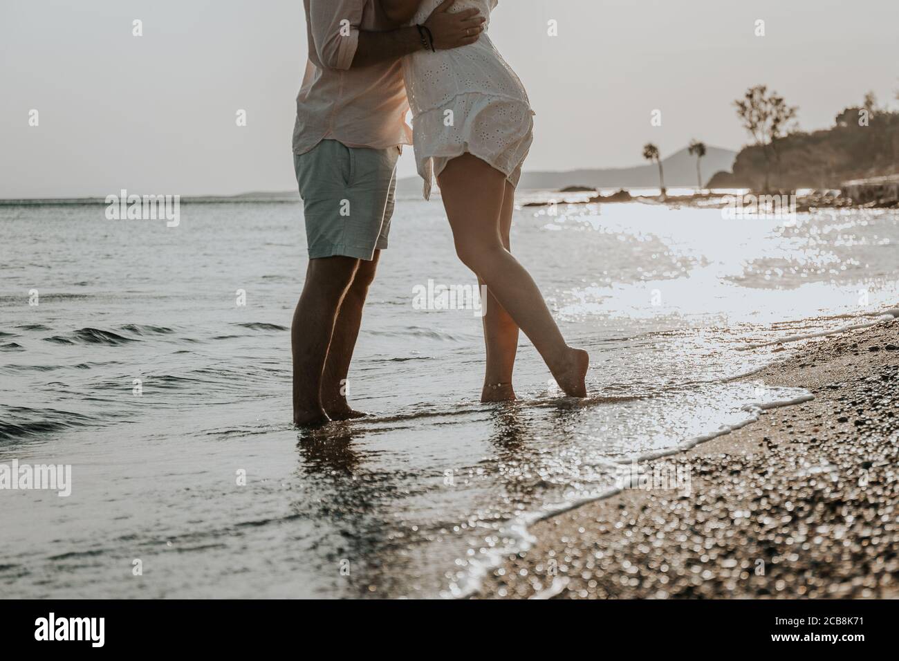 Le gambe sulla spiaggia. Piedi spa. Una giovane coppia amorevole abbraccia e bacia sulla spiaggia al tramonto. Due amanti, l uomo e la donna a piedi nudi vicino all'acqua. Estate ho Foto Stock