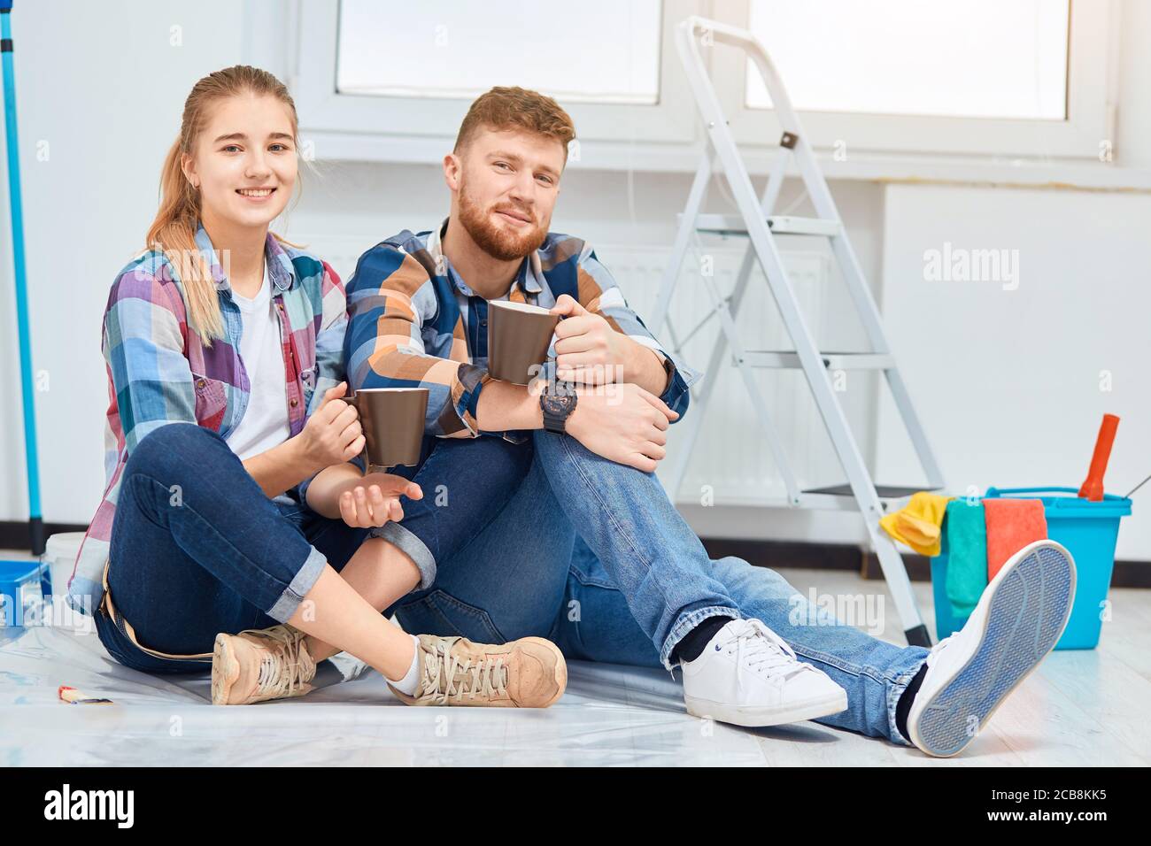 Giovane famiglia di decoratori di casa che si raffredda in camera vuota preparata per la pittura, seduto tra gli attrezzi, che sono sempre necessari durante il tempo di riparazione instru Foto Stock