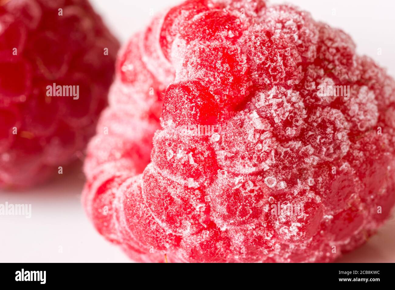 Macrofotografia di un lampone rosso fresco recuperato con il gelo. Un altro lampone sullo sfondo Foto Stock