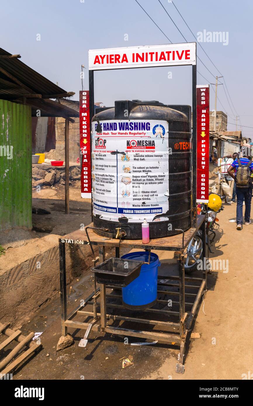 Un grande serbatoio d'acqua di plastica con un cartello di lavaggio a mano libera su di esso per combattere il coronavirus dal lato di una strada sterrata, Nairobi, Kenya Foto Stock