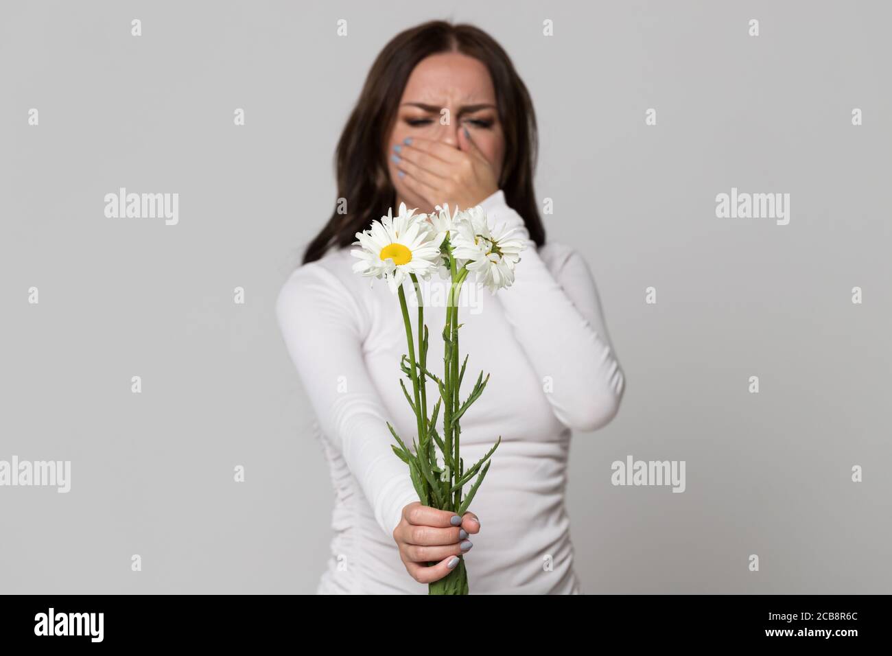 Studio ritratto di bruna femmina che ricopre il naso, avendo una reazione allergica ai fiori camomilla, fuoco selettivo. Allergia. Foto Stock