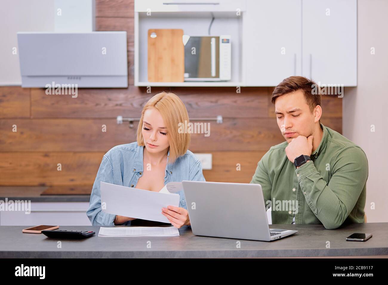 giovane donna caucasica e uomo che indossa abbigliamento casual verificare la situazione finanziaria in famiglia, facendo fattura verficitaion utilizzando computer portatile, carte e calcolatrice Foto Stock