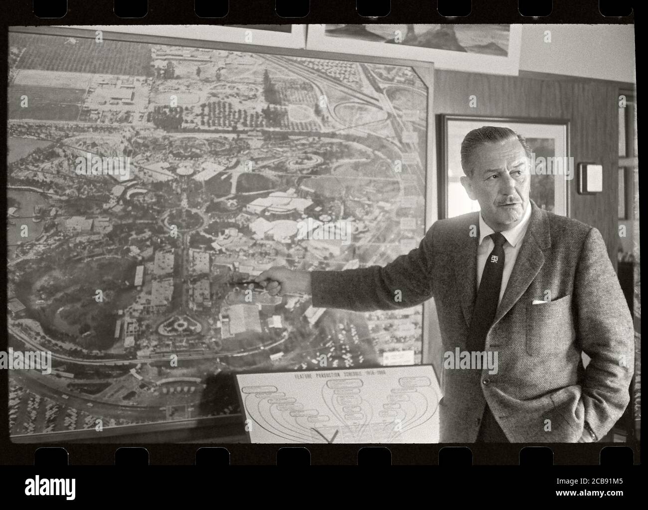 Il pioniere del cinema Walt Disney punta alla mappa di Disneyland. Un grafico sotto la mappa legge, Feature Production Timeline 1954 -1964. Immagine da negativo 35 mm. Foto Stock
