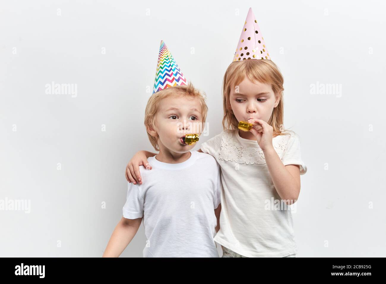 due bambini carini che usano fischietti da festa, indossando cappelli da  festa su uno sfondo bianco, felice infanzia, primo piano ritratto, vacanza  Foto stock - Alamy