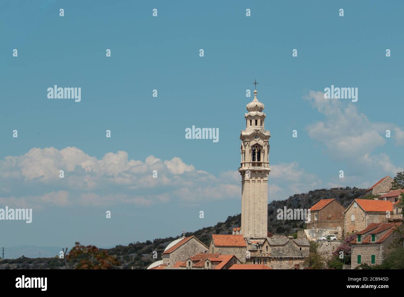 Alto campanile in un piccolo villaggio di Lozisca sull'isola di Brac, Croazia. Bella torre cristiana che si erge sopra gli edifici antichi Foto Stock