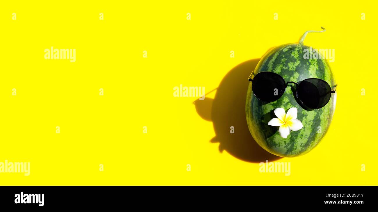 Cocomero con occhiali da sole e plumeria o fiore frangipani su sfondo giallo. Spazio di copia Foto Stock