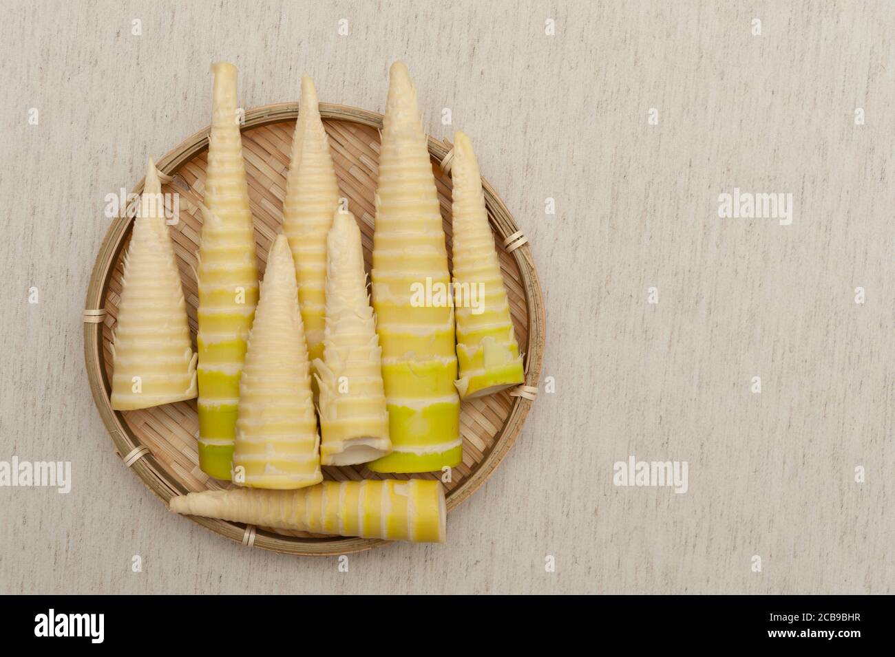 Cucina Giapponese - Shoot di bambù grezzo sbucciato in un vassoio di bambù intrecciato isolato su sfondo beige. Vista dall'alto. Spazio di copia. Foto Stock