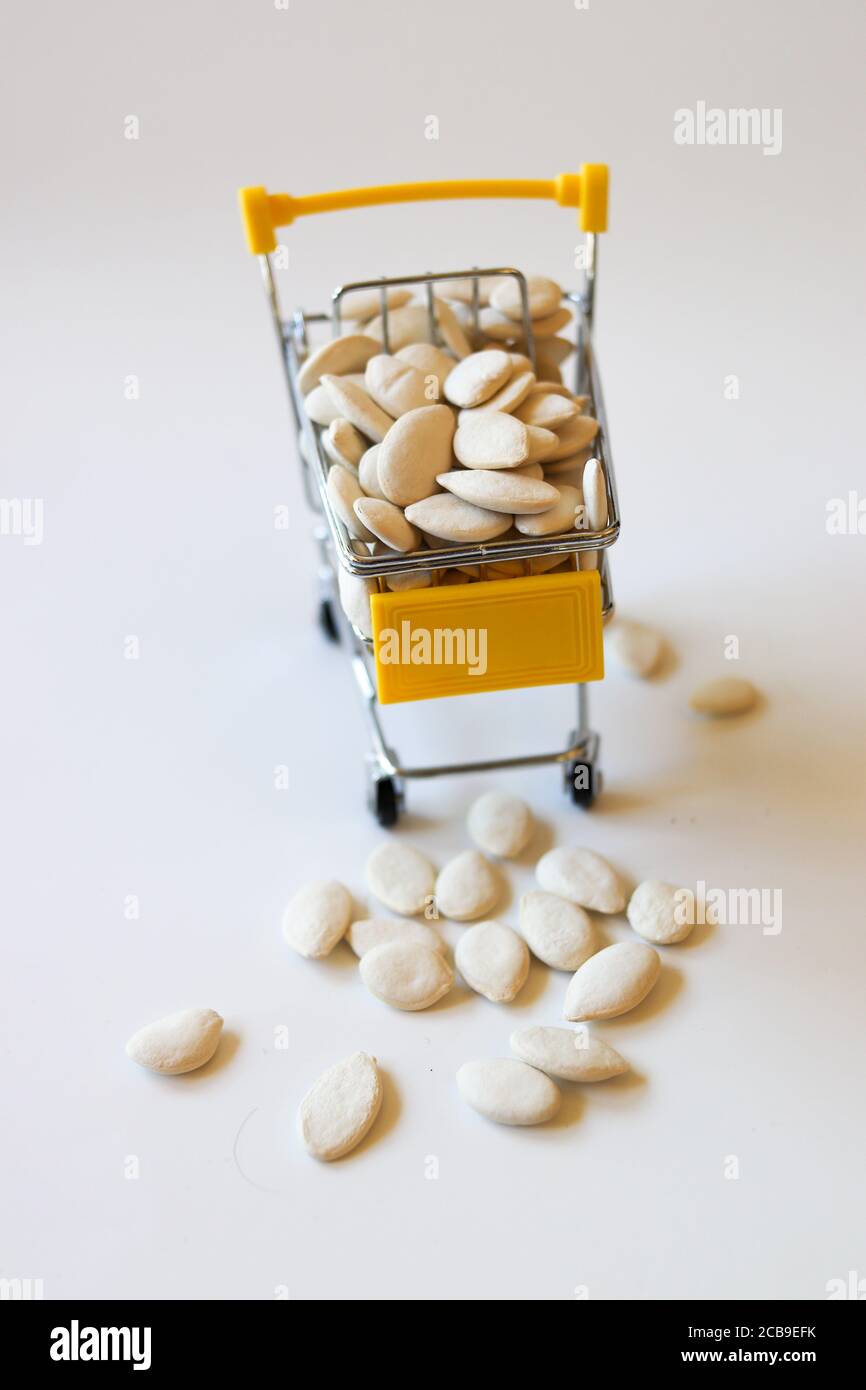 Carrello della spesa giallo in miniatura con cestino pieno di semi di zucca Foto Stock