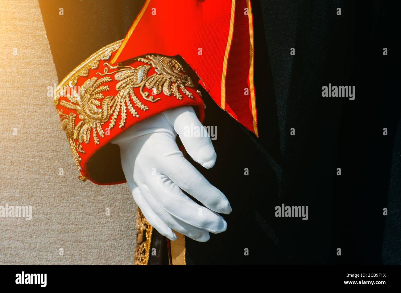 Abiti storici da uomo neri con intarsi decorati in rosso e oro sulla manica, una mano in guanti bianchi Foto Stock