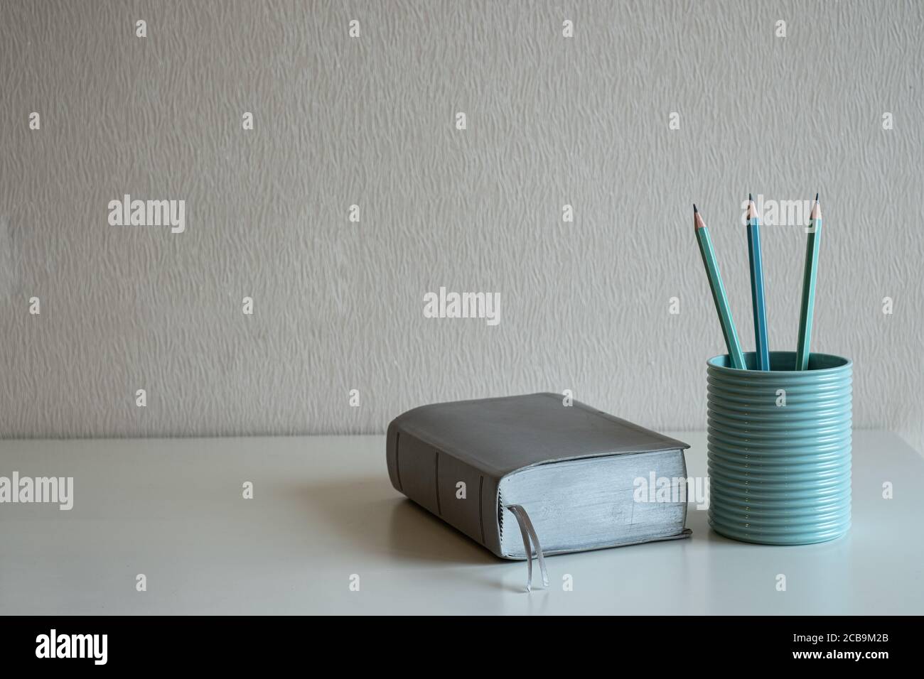 Un libro e matite pastello nel vetro blu sopra la scrivania su sfondo grigio Foto Stock