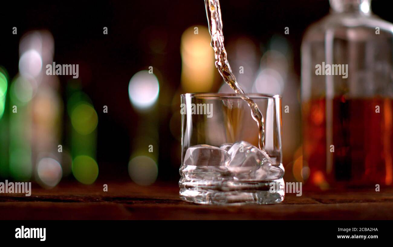 Versare il whisky nel bicchiere. Posto su tavolo di legno. Bassa profondità di messa a fuoco Foto Stock
