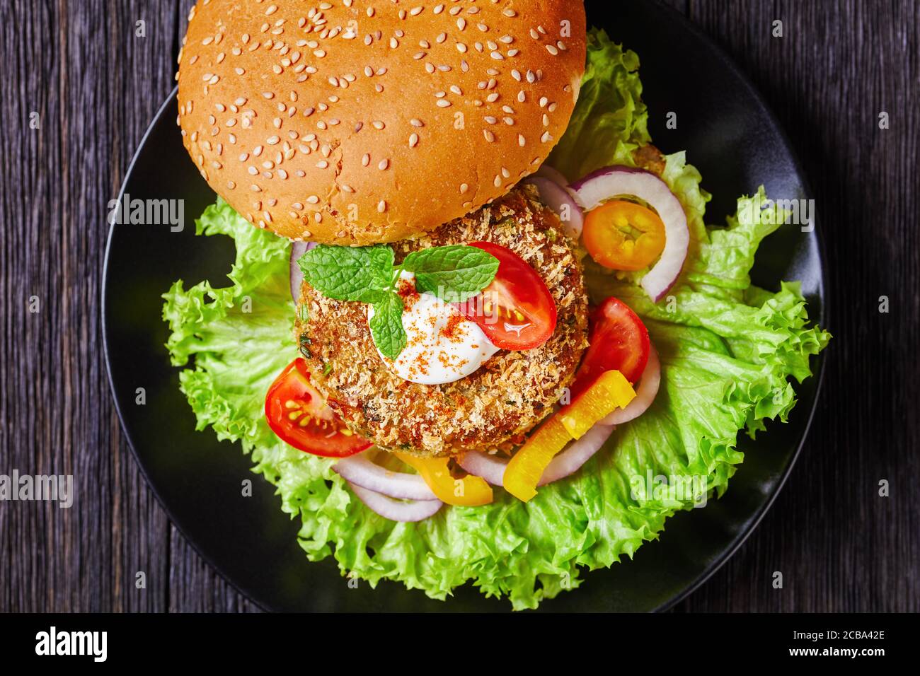 Vegan Chickpea Veggie Burger con panino appena sfornato con semi di sesamo e insalata di lattuga su un piatto nero, piatto, primo piano, macro Foto Stock