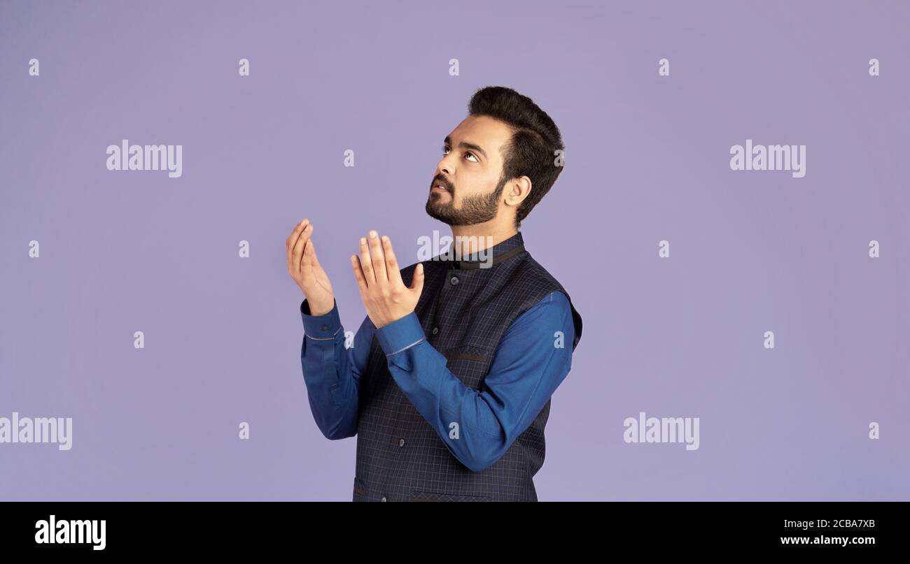 L'uomo indiano prega a Dio, chiedendo aiuto o perdono su sfondo lilla Foto Stock
