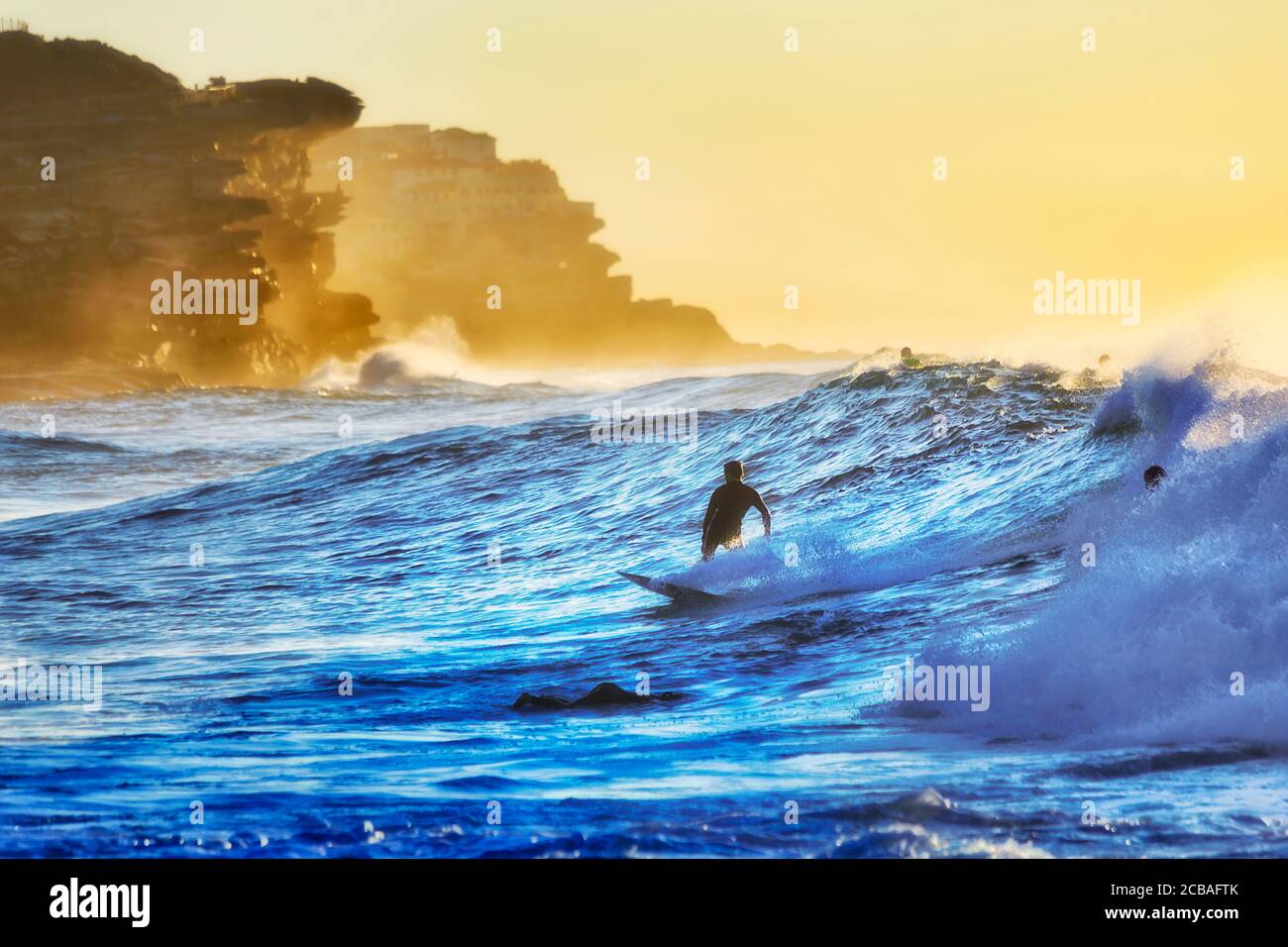 Un gruppo di surfisti che galleggiano e cavalcano un'onda alla spiaggia di Bronte, nella periferia orientale di Sydney, costa del Pacifico all'alba. Foto Stock