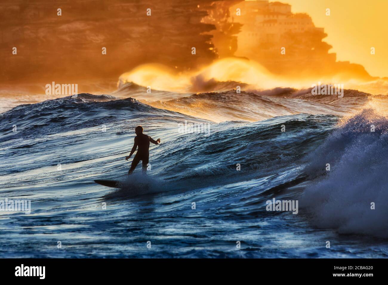 Surfer maschile singolo irriconoscibile scivola l'onda alla spiaggia di Bronte di Sydney Eastern Suburbs sulla costa dell'oceano Pacifico in sole mattine. Foto Stock