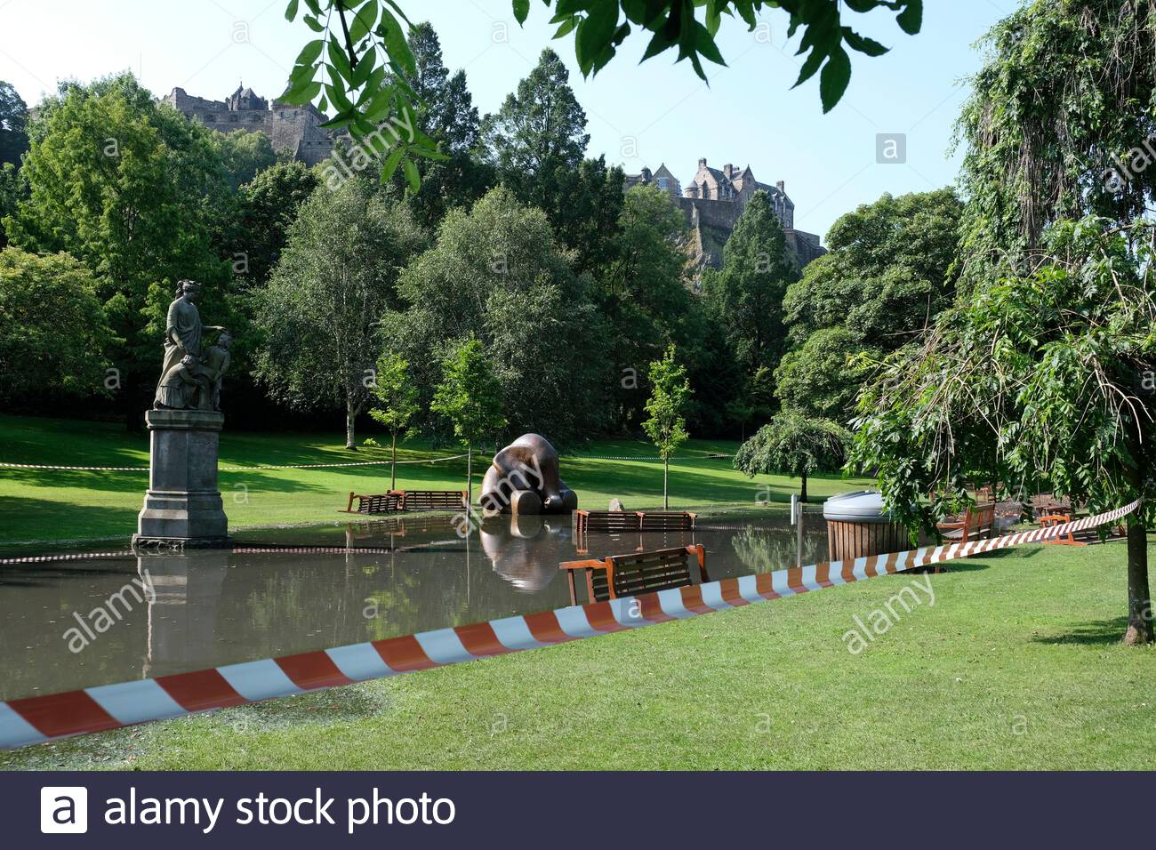 Edimburgo, Scozia, Regno Unito. 12 agosto 2020. Il tempo soleggiato sostituisce le tempeste notturne che lasciano i West Princes Street Gardens allagati e cordonati al pubblico. Scultura in bronzo elefante intrappolata nelle acque alluvionali. Vista sul Castello di Edimburgo. Credit: Craig Brown/Alamy Live News Foto Stock