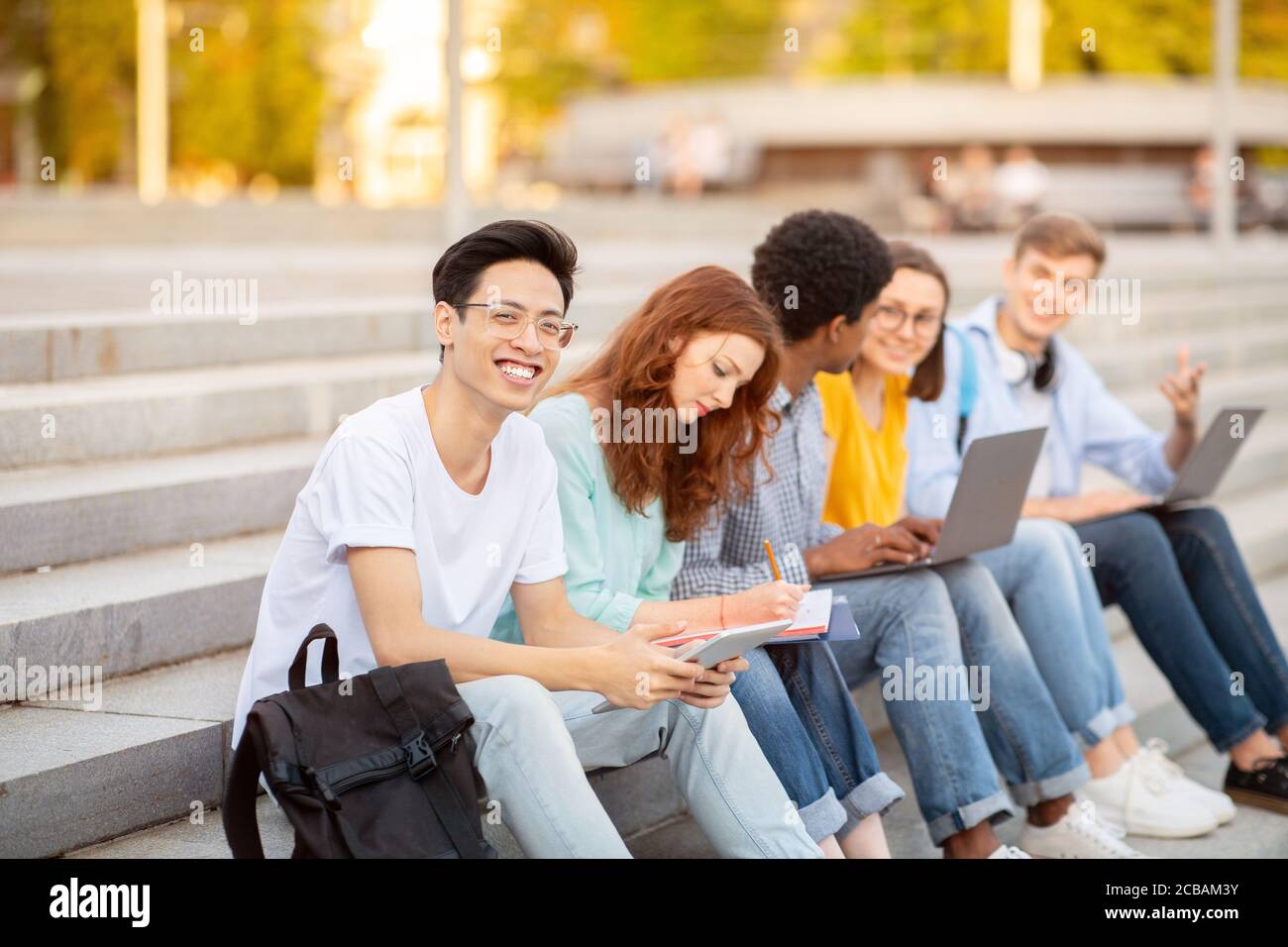 Ragazzo asiatico che studia all'aperto con i suoi amici Foto Stock
