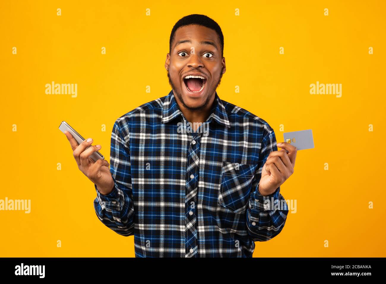 Uomo eccitato con smartphone e carta di credito gridando, sfondo giallo Foto Stock