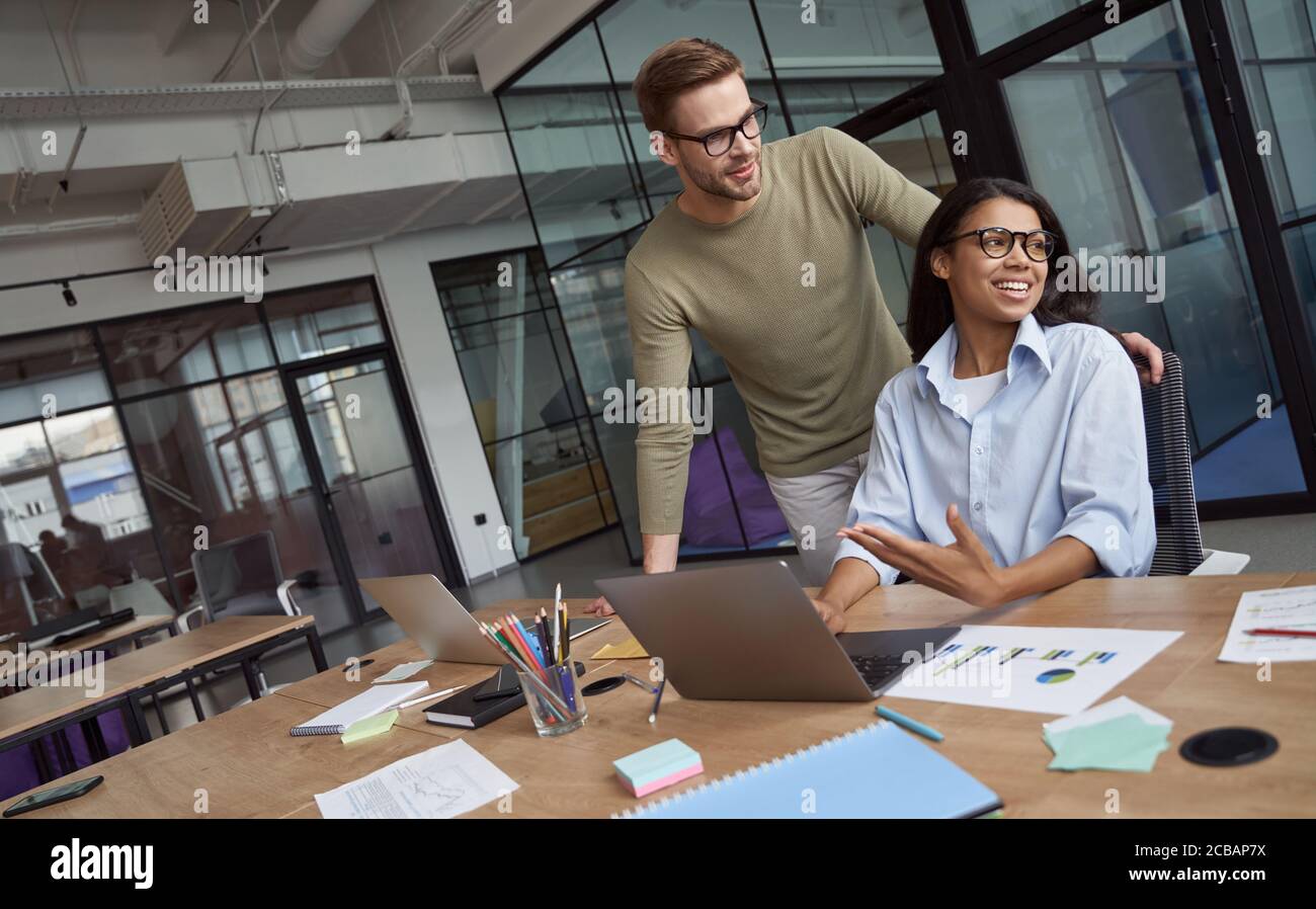 Insegnare ai nuovi dipendenti. Gruppo di due colleghi felici che lavorano insieme nel moderno spazio dei colleghi, parlando e comunicando Foto Stock