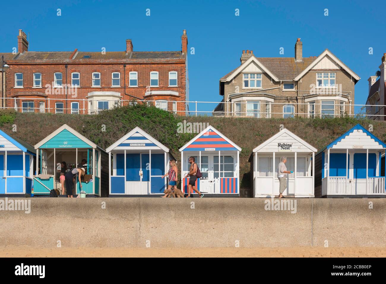 Suffolk mare, vista in estate di persone che camminano attraverso colorate capanne sulla spiaggia lungo il lungomare di Southwold sulla costa di Suffolk, Inghilterra, Regno Unito Foto Stock
