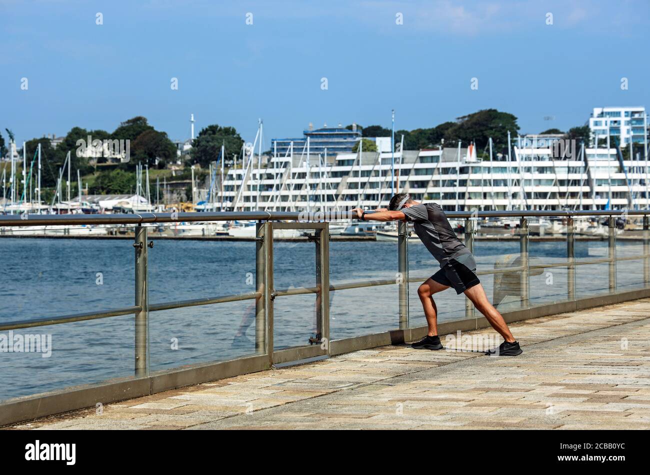 Un jogger prende una pausa dalla corsa per un'attività contro le ringhiere del muro del fiume al Royal William Yard a Stonehouse Plymouth. Precedente MOD Vitual Foto Stock