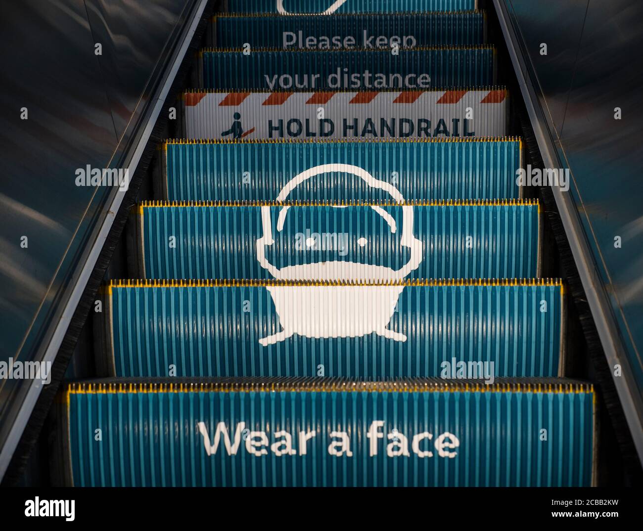 Indossa un messaggio Face Mask, su Escalators, Reading Rail Station, Reading, Berkshire, Inghilterra, Regno Unito, GB. Foto Stock