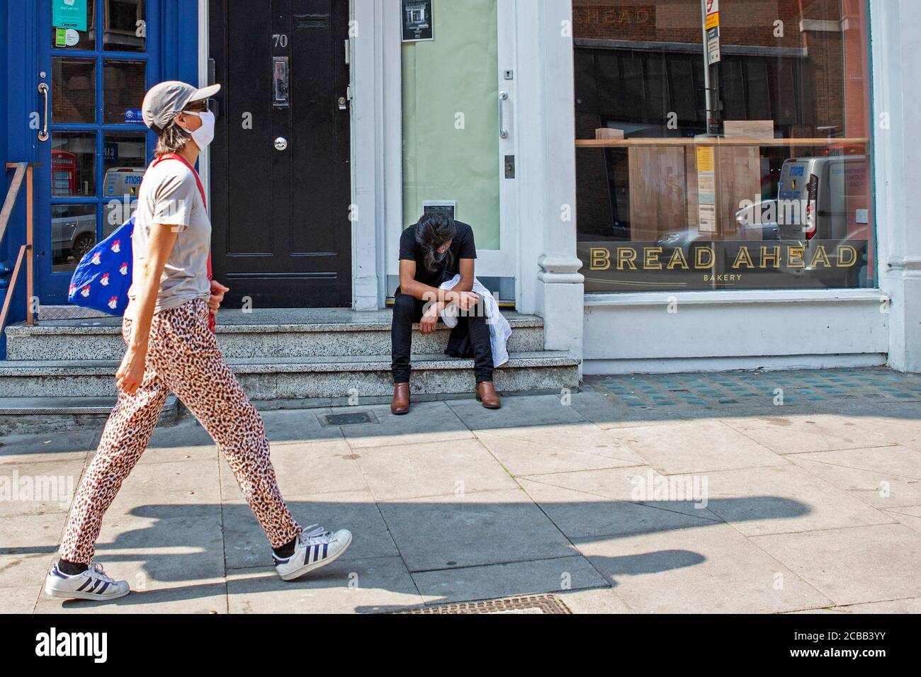 Un uomo si siede stanco fuori da un negozio che è chiuso in Hampstead High Street come affari vicino tutto il Regno Unito a causa del Coronavirus o Covid-19. Foto Stock